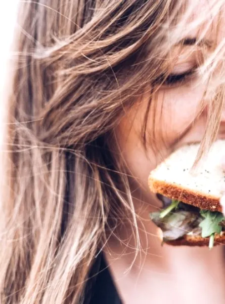 Girl eating a sandwich with wind blowing her hair