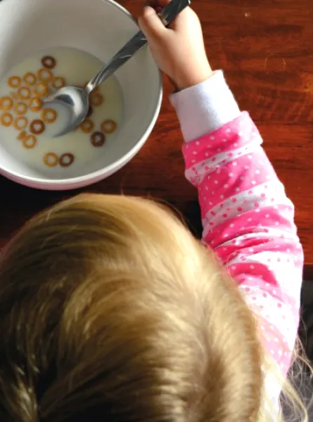 Child with a pink shirt eating cereals with milk