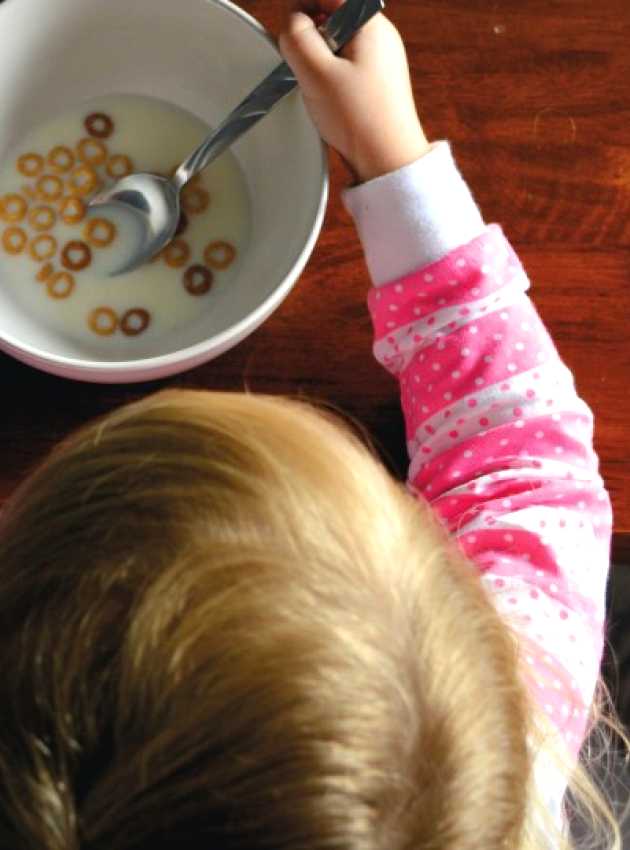 Child with a pink shirt eating cereals with milk