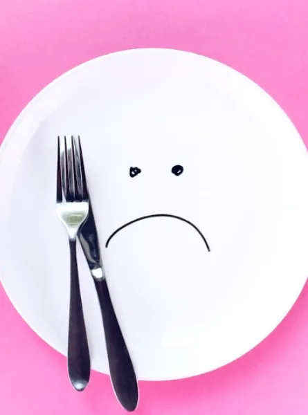 sad plate with a fork and a knife on a pink background