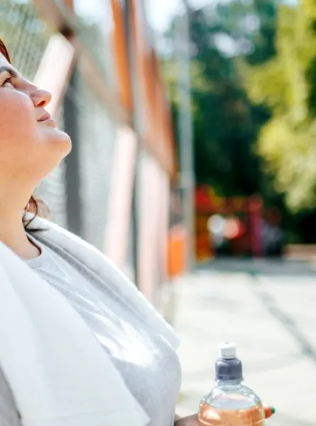 Woman taking a break after outdoor exercise, holding a water bottle, symbolizing a weight loss journey