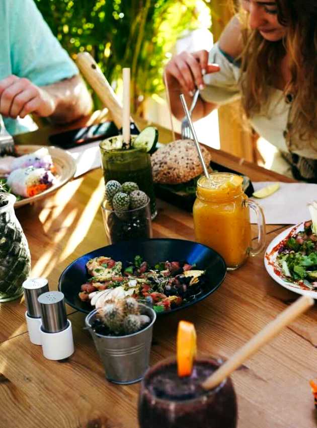 Group of people enjoying a meal with fresh salads, smoothies, and bread at an outdoor table.