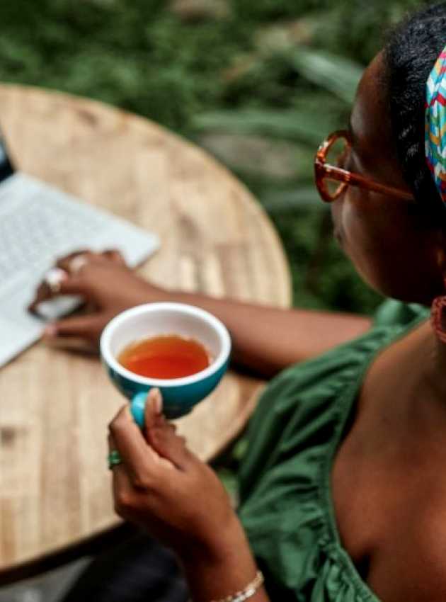 A woman drinking her hot tea while working outside in front of her computer.