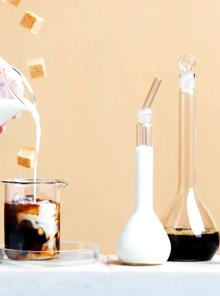 Main versant du lait dans un café glacé avec des morceaux de sucre flottants - Hand pouring milk into iced coffee with floating sugar cubes
