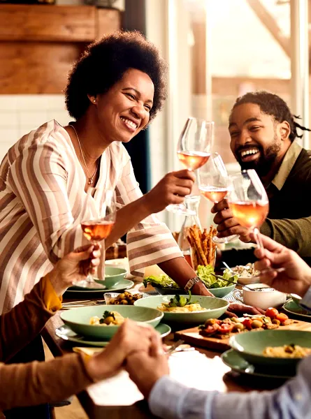 Groupe d'amis multiculturels trinquant avec des verres de vin rosé autour d'un repas - Multicultural group of friends toasting with glasses of rosé wine around a meal