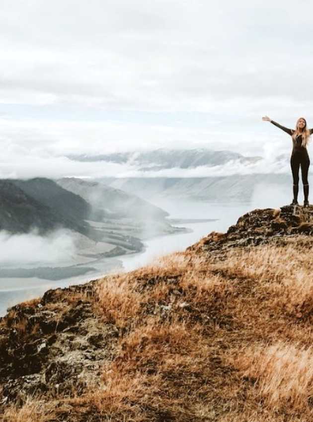 Une femme avec les bras en croix au sommet d'une montagne.