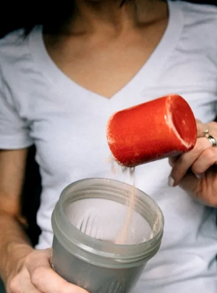 A woman putting a cup of protein powder in the blender