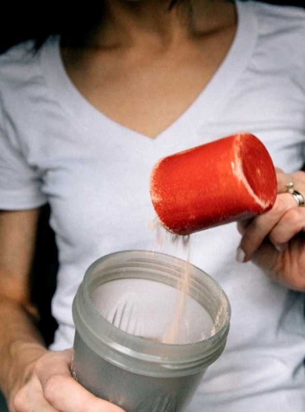 A woman putting a cup of protein powder in the blender