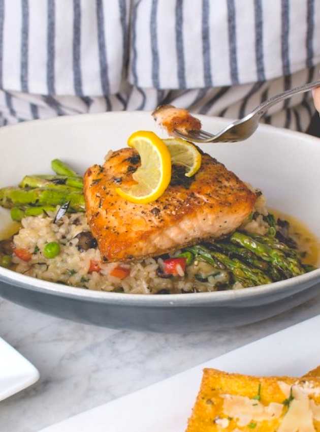 Woman eating salmon served on a bed of asparagus and rice 