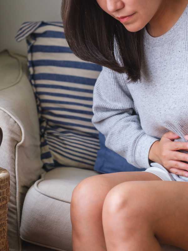 Femme souffrant de maux d'estomac et de douleurs abdominales assise sur un canapé à la maison
